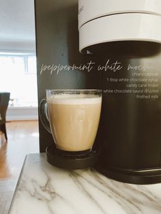 a cup of coffee sitting on top of a counter next to a black machine with white writing