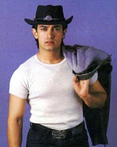 a man wearing a hat and holding a jacket over his shoulder while standing in front of a purple background