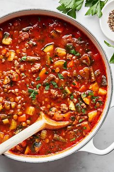 a pot filled with stew and vegetables on top of a white counter next to a wooden spoon