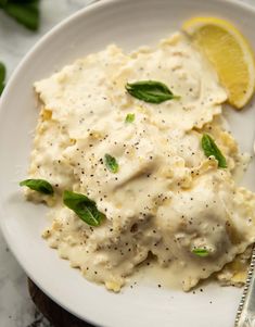 a white plate topped with mashed potatoes covered in gravy next to a lemon wedge