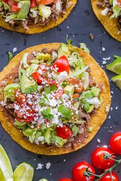 three tacos topped with meat, lettuce and tomatoes on a blue surface