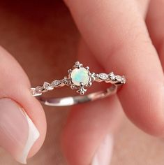 a woman's hand holding a white opal and diamond ring