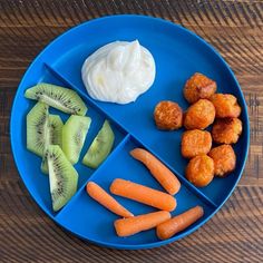 a blue plate topped with kiwi, carrots and cucumbers next to yogurt