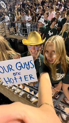 two girls in green shirts and cowboy hats holding up a sign that says our guys are hotter