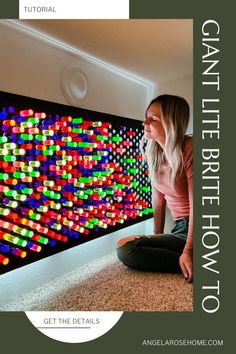 a woman sitting on the floor in front of a large painting with colorful lights behind her