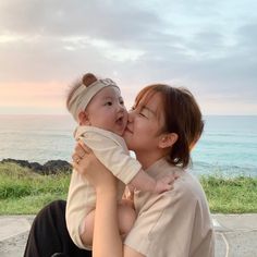 a woman holding a baby in her arms near the ocean