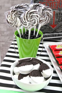 a table topped with chocolate covered cookies and lollipops next to a green cup filled with oreos