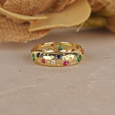 a gold ring with multicolored stones on it and a flower in the background