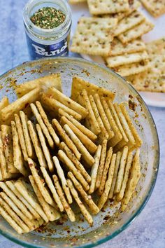 some crackers are in a glass bowl with seasoning on the table next to them