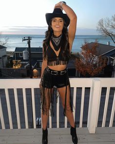 a woman in a black top and fringe skirt posing on a porch near the ocean