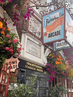 the outside of a restaurant with flowers hanging from it's ceiling and signs on the wall