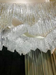 a large chandelier hanging from the ceiling in a room with curtains and drapes