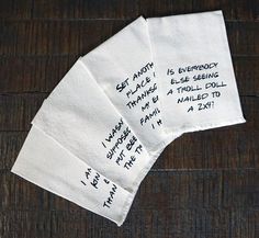 three napkins with writing on them sitting on top of a wooden table next to each other