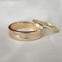 two gold wedding rings with baguettes on top of each other, sitting on a white cloth