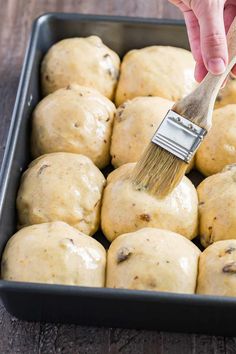 a person holding a paint brush in a pan filled with rolls and doughnuts