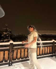 a man standing on top of a snow covered roof next to a wooden fence at night