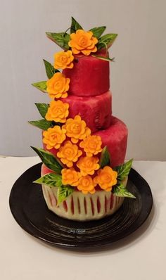 a three tiered cake decorated with flowers on a black plate and white tablecloth