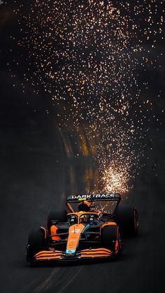 an orange race car driving down the road with fireworks in the air behind it and on to the ground