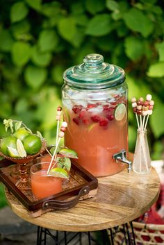 a wooden table topped with glasses filled with liquid and fruit next to a jar full of water