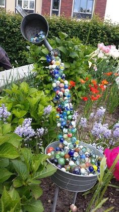 a garden filled with lots of colorful flowers and plants next to a metal bucket full of marbles