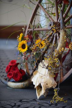 flowers and skulls are arranged on the floor in front of a wheelbarrow that is decorated with vines