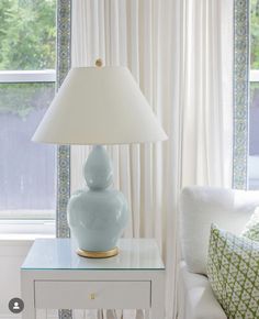 a blue lamp sitting on top of a table next to a white couch in front of a window