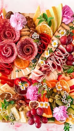 an assortment of different types of cheeses and meats on a platter with flowers