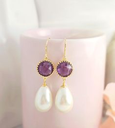 a pair of earrings with pearls and amethorate on them sitting next to a cup