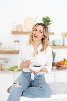 a woman sitting on top of a counter holding a bowl