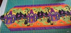 a purple and green place mat with halloween houses on it next to a pair of scissors