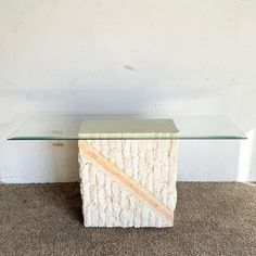 a glass and stone table on carpeted floor with white wall in the back ground