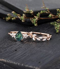 two rings with green and white stones sitting on top of a wooden table next to greenery