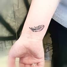 a woman's wrist with a small feather tattoo on her left hand and the word love written below it