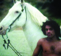 a shirtless man standing next to a white horse with long hair on it's head