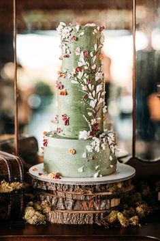 a three tiered green cake with flowers on it sitting on top of a table