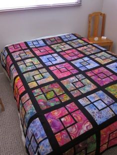 a bed with a colorful quilt on top of it next to a chair and window