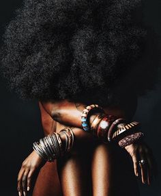 an african woman with large black hair and bracelets on her arm, sitting in front of a dark background