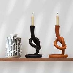 three candles sitting on top of a wooden shelf next to a vase and candle holder