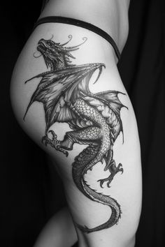 a black and white photo of a woman's thigh with a dragon tattoo on it