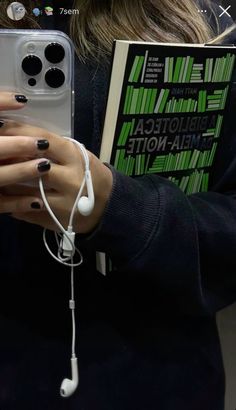 a woman with black and white nail polish holding a cell phone in her hand while wearing headphones