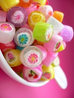 a white bowl filled with colorful candies on top of a pink table next to a plastic spoon