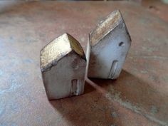 two small metal buildings sitting on top of a table next to each other and one is broken