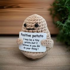 a crocheted stuffed animal holding a sign that says positive potato i may be a tiny potato but i believe in you go to do your thing