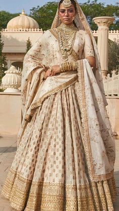 a woman in a white and gold bridal gown posing for the camera with her hands on her hips