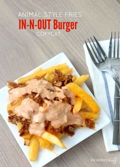 a white plate topped with fries covered in gravy next to a fork and knife