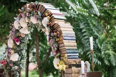 an arch made out of books is decorated with flowers and candles for a wedding ceremony