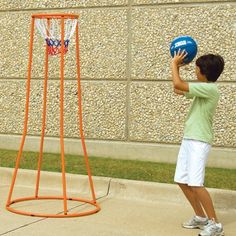 a young boy holding a blue basketball in front of an orange hoop on the sidewalk