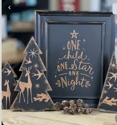 three wooden christmas trees with gold foil on them and a black framed sign that says one child, one star, one night