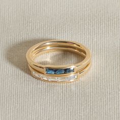 two gold rings with blue and white stones on them sitting on a beige cloth surface