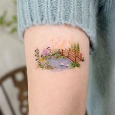 a woman's arm with a small watercolor landscape tattoo on the left forearm